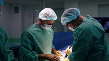 Gözlük takan baş cerrah ameliyatta modern cerrahi aletler kullanıyor. Metal aletleri tutan iş arkadaşı yardımcıları.