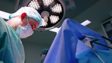 Maskeli ve şapkalı orta yaşlı erkek doktor. İşle meşgul bir cerrahın düşük açılı portresi..