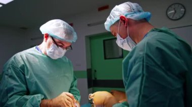 Beyaz erkek doktorlar operasyonda metal aletler kullanıyorlar. Asistan enstrüman ve malzemeleri cerrahlara verir..