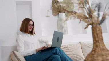 Kafkasyalı kadın kanepede rahatça oturuyor. Uzaktan kumandayla çalışan bir bayan dizüstü bilgisayarı kucağında tutuyor..