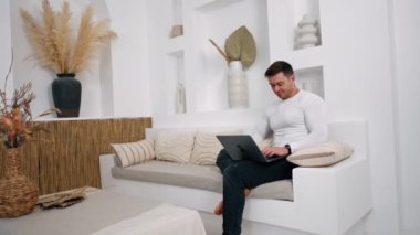Aydınlık bir odada oturan odaklanmış beyaz bir erkek. İşadamı bilgisayarını uzaktan kumandayla evden alıyor..