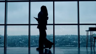 Erkek ve kadın işçilerin siluetleri birbirine yaklaşıyor. Erkek kahve içer ve kadın telefonda konuşur. Arkaplanda panoramik pencere.