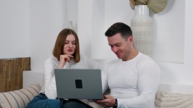 Kanepede oturan beyaz bir çift dizüstü bilgisayar ekranına bakıyor. Rahat atmosferde uzak bir iş.