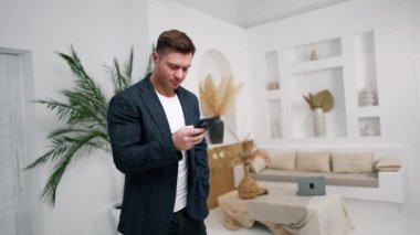 Siyah saçlı, ceketli bir erkek telefonuna bakıyor. Adam interneti arıyor, bir numara arıyor ya da mesaj yolluyor.