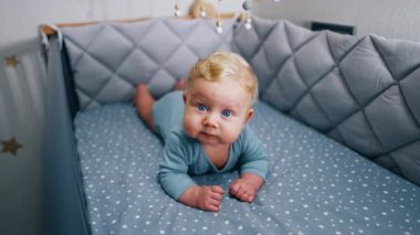Sevimli tombul yanaklı beyaz bebek beşikte huzur içinde yatıyor. Sevimli mavi gözlü bebek bir şeyler çiğniyor..