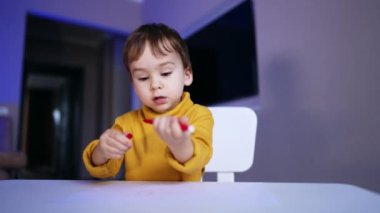 Masada oturan güzel beyaz çocuk. Küçük oğlan keçeli kalem ve kalem kapağıyla uğraşıyor. Düşük açı görünümü.
