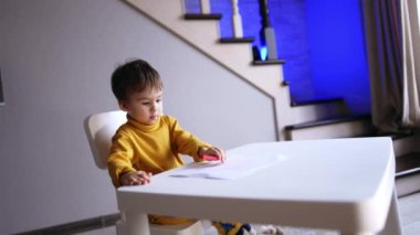 Küçük tatlı çocuk, masaya oturur. Sevimli erkek bebek kâğıdı açmadan kalemle oynuyor..
