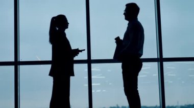 İki meslektaş karşı karşıya duruyor. Kadın ve erkeğin siluetleri pencerenin önünde konuşuyorlar. Düşük açı görünümü.