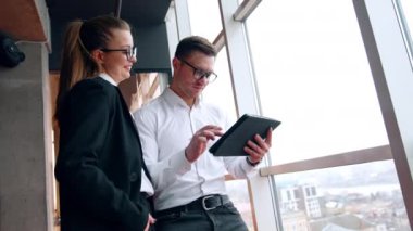 Kadın ve erkek çalışanlar büroda. Kadın, üzerinde çalışan adamın elindeki I-pad 'e bakıyor. Düşük açı görünümü.