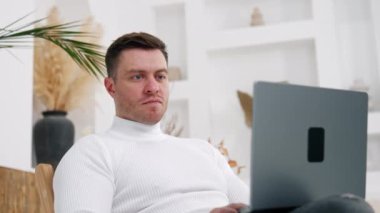 Beyaz gömlek giyen ciddi bir beyaz adam laptopuna dikkatlice bakıyor. Ofisten uzakta rahat bir iş yeri. Düşük açı görünümü.