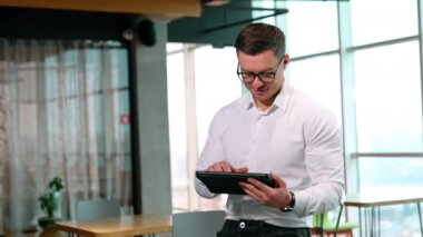 Modern sektörde dijital teknolojiyi kullanmak. Gözlüklü adam geniş bir ofiste I-pad 'inde çalışıyor..