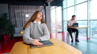 Dizüstü bilgisayarında yatan uzun saçlı kadın işten yorgun düşmüş. Kadın kollarını yana açıyor ve işe dönmek için aletini açıyor..