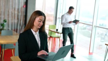 Başarılı modern iş kadını dizüstü bilgisayarda yazıp kapatıyor. Bulanık arka plandaki adam I-pad 'de çalışıyor..