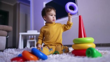 Güzel beyaz çocuk oyuncak piramidini monte ediyor. Sevimli erkek bebek evde huzur içinde oynuyor..