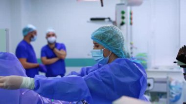 Üniformalı kadın doktor tıbbi ekipmanların kablo ve tüplerini çözüyor. İki erkek doktor arka planda bulanık duruyor..
