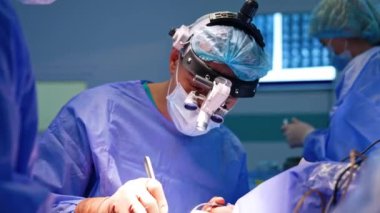 Cerrahi hoparlör takan deneyimli erkek beyin cerrahı metal alet kullanır ve asistana verir. Tıbbi ekiple birlikte ameliyat yapan bir doktorun portresi..