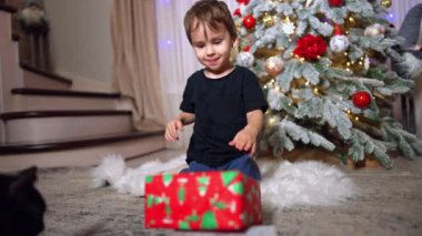 Meraklı çocuk Noel ağacının yanında parlak hediye kutularıyla oynuyor. Güzel bebek tatil için hediye bekliyor..