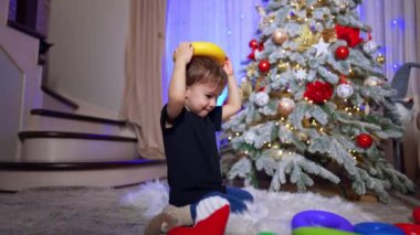 Komik çocuk oyuncağı kafasına koyuyor. Beyaz çocuk Noel için dekore edilmiş odada oynuyor..