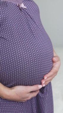 Tanımlanamayan hamile bir kadın koca karnını sevgiyle okşuyor. Gecelik giyen hamile kadın yatak odasında yarı açık duruyor. Kapatın. Dikey video