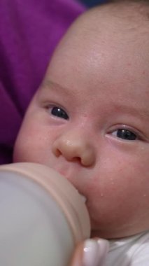 Sevimli yeni doğmuş bebek biberonla besleniyor. Anne çocuğunu kucağına alıp şişeden besliyor. Kapatın. Dikey video