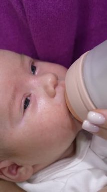 Annesinin ellerinde dinlenen ve biberonla beslenen yeni doğmuş güzel bir çocuk. Küçük çocuk gözlerini kapar ve yavaş yavaş uykuya dalar. Kapatın. Dikey video