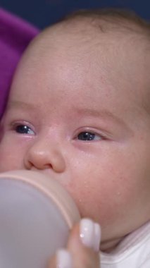 Şişeden süt emen tatlı bir bebek. Bebek gözlerini kapar ve yemek yerken uyuyakalır. Anneciğin ellerindeki çocuk kapat. Dikey video