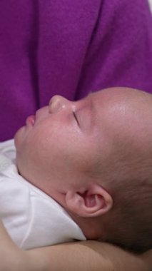 Tatlı çocuk uyuyor ve sonra yavaşça uyanıyor ve ellerini sallıyor. Bebek, annenin ellerinde tatlı tatlı esniyor. Kapatın. Dikey video