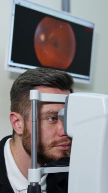 Göz hekimliği kliniğindeki hasta. Adam tıbbi tedavi için cihazların içine bakıyor. Göz doktorunda gözlerini kontrol eden genç bir adam. Dikey video