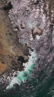 Okyanusun güneşli sularında parlayan California sahilindeki kayaları yıkayan. İnsansız hava aracı görüntüleri, üzerinde otoyol olan kayalık sahil şeridine iniyor. Dikey video