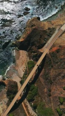 Köprü ile birbirine bağlı dağlardaki yolların görüntüsü. Kaliforniya 'nın Rocky sahili. Hava perspektifinden güzel mavi okyanusları var. Dikey video