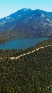 Etrafında çam ağaçları büyüyen muhteşem dağ manzarası. Dağlarda saklanan küçük mavi bir göl. Üst Manzara. Dikey video