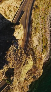 Otoyollarda tünelleri olan yüksek kayalar. Güneşli bir günde dağlık bir göl manzarası. Üst Manzara. Dikey video