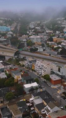 San Francisco 'daki karmaşık yollar trafiği yoğun. Şehir panoraması yavaş yavaş beyaz sisle kaplanıyor. Hava görüntüsü. Dikey video