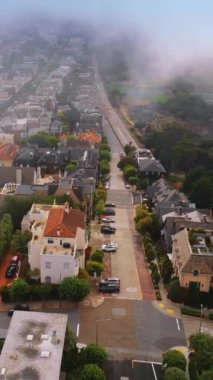 Modern San Francisco 'da güzel, çeşitli evler. Yoğun sis şehrin üzerinde yavaşça gökyüzünü kaplıyor. Hava görüntüsü. Dikey video