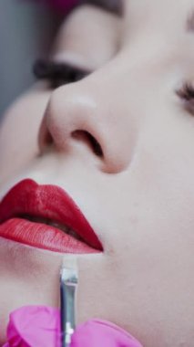 Mükemmel makyajlı bir kadının güzel yüzü. Dudak dövmesinin estetik prosedürü. Dudak makyajı yapan bir güzellik uzmanı. Dikey video