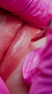 Kalıcı makyaj dudakları prosedürü. Elleri lateks eldivenli yetenekli bir kozmetik uzmanının dudaklarına dövme makinesiyle pigment makyaj uygulaması. Makro atış. Dikey video