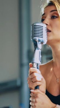 Çekici bir kadın mikrofona şarkı söylüyor. Profesyonel şarkıcı mikrofonun başında duruyor ve canlı müzik yapıyor. Ağır çekim. Dikey video