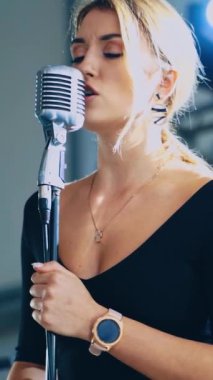 Sarışın kadın mikrofona şarkı söylüyor. Sahnede durup şarkı söyleyen çekici bir şarkıcı. Müzikal eğlence. Dikey video