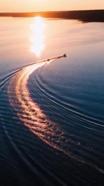 Gün batımında güzel nehirde bir tekne. Akşam güneşinden gelen altın yola karşı gemiler hareket ediyor. Hava görüntüsü. Dikey video