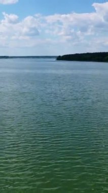 Mavi gökyüzünün altında akşam suyu. Güzel geniş nehir manzarası. Tarlalar ve ormanlar arasında sakin bir nehir. Hava uçuşu. Dikey video