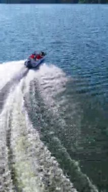 Sürat teknesi nehir boyunca koşar. Mavi nehir suyundaki beyaz köpüğün doğa arka planındaki teknenin arkasındaki güzel manzarası. Hava görüntüsü. Dikey video