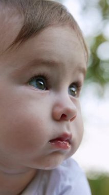 Bir çocuğun sevimli yüzü yana bakıyor. Dışarıda kalan tatlı bir bebek. Kapatın. Arkaplan bulanık. Dikey video