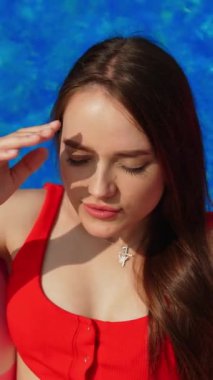 Havuzdaki yüzme havuzunda kırmızı mayo giymiş dövmeli kız. Esmer, yazın boş vakitlerinde güneşin tadını çıkarıyor. Dikey video