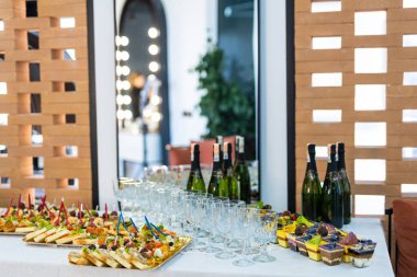 Modern bir ortamda beyaz bir masa abur cubur, şarap ve tatlılarla doludur..