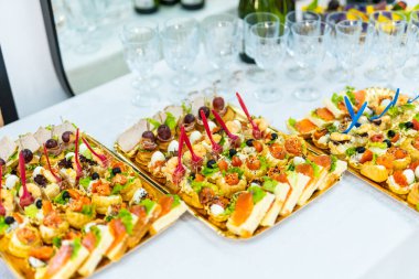 Beyaz çarşaflı bir masa seti üç altın tepside çeşitli küçük, lezzetli aperatifler barındırır..