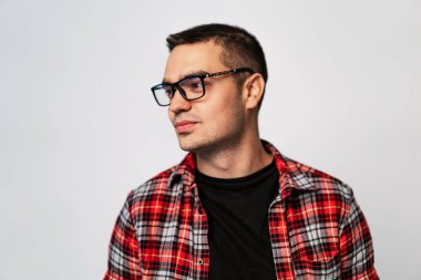 Kısa, koyu renk saçlı, gözlüklü ve siyah tişörtlü bir adam kameradan uzağa bakıyor..