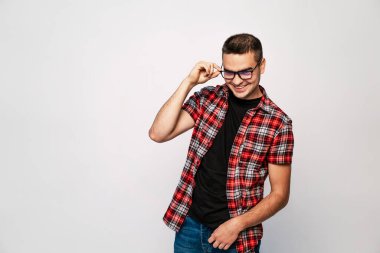 Kırmızı ve siyah ekose gömlek giyen bir adam gözlüğünü ayarlarken hafifçe gülümsüyor, yana bakıyor..