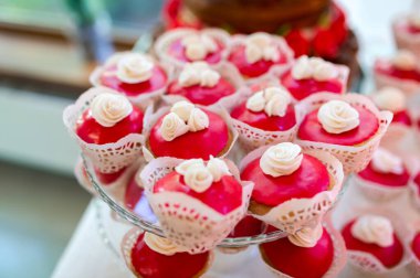 Beyaz fontane güllerle kaplı kırmızı kadife keklerin yakın plan görüntüsü, beyaz altlıklı cam pasta standında düzenlenmiştir..