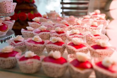 Cam bir yüzeye yerleştirilmiş dantel ambalajlı pembe ve beyaz kapkekler..