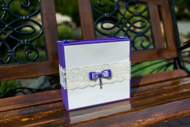 Beyaz dantel kurdeleli mor bir hediye kutusu ve ahşap bir bankta oturan mor bir fiyonk..